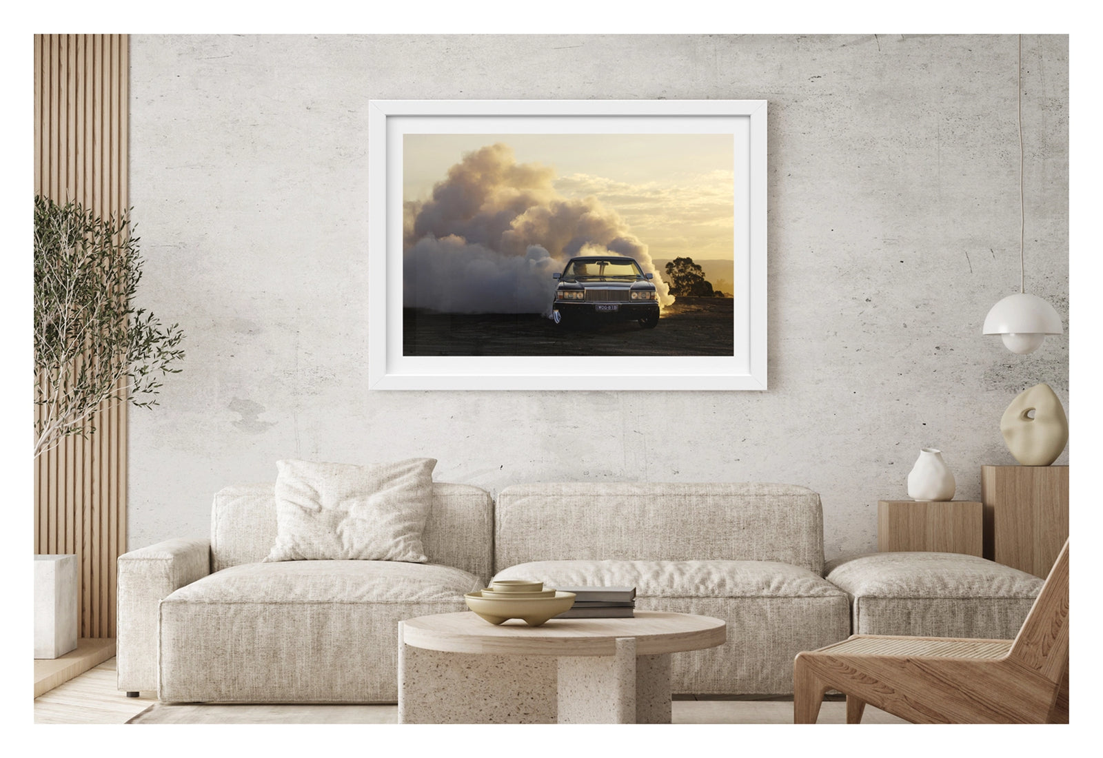 Framed in white. Front view of a WB Holden ute performing a poetic burnout at golden hour, smoke billowing behind it like an approaching thunderstorm. Fading sunlight catches the haze and chrome as the car stays ahead of its own chaos. Shown in a contemporary living space. Fine art print by Simon Davidson.