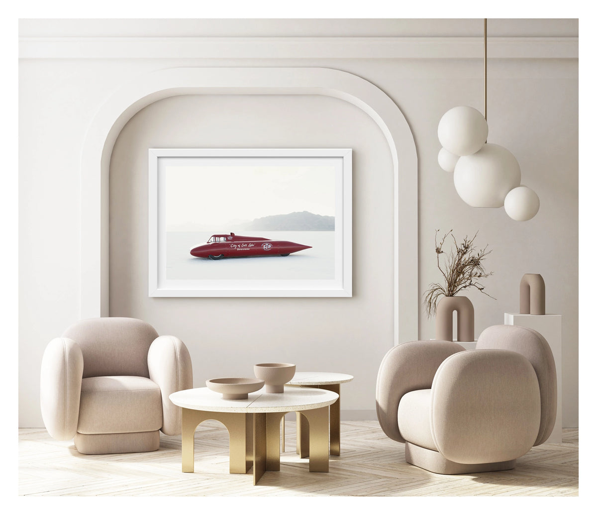 Framed in white, hanging in a contemporary living space. A red vintage streamliner named City of Salt Lake and sponsored by STP and Firestone sits on the Bonneville Salt Flats, its long streamlined shaped body tapering to a sharp nose point with a small raised cockpit canopy above. The elegant mid century streamliner form glows deep red against the bleached white salt and pale hazy mountains dissolving into the horizon behind it. Fine art colour photographic print by Simon Davidson.