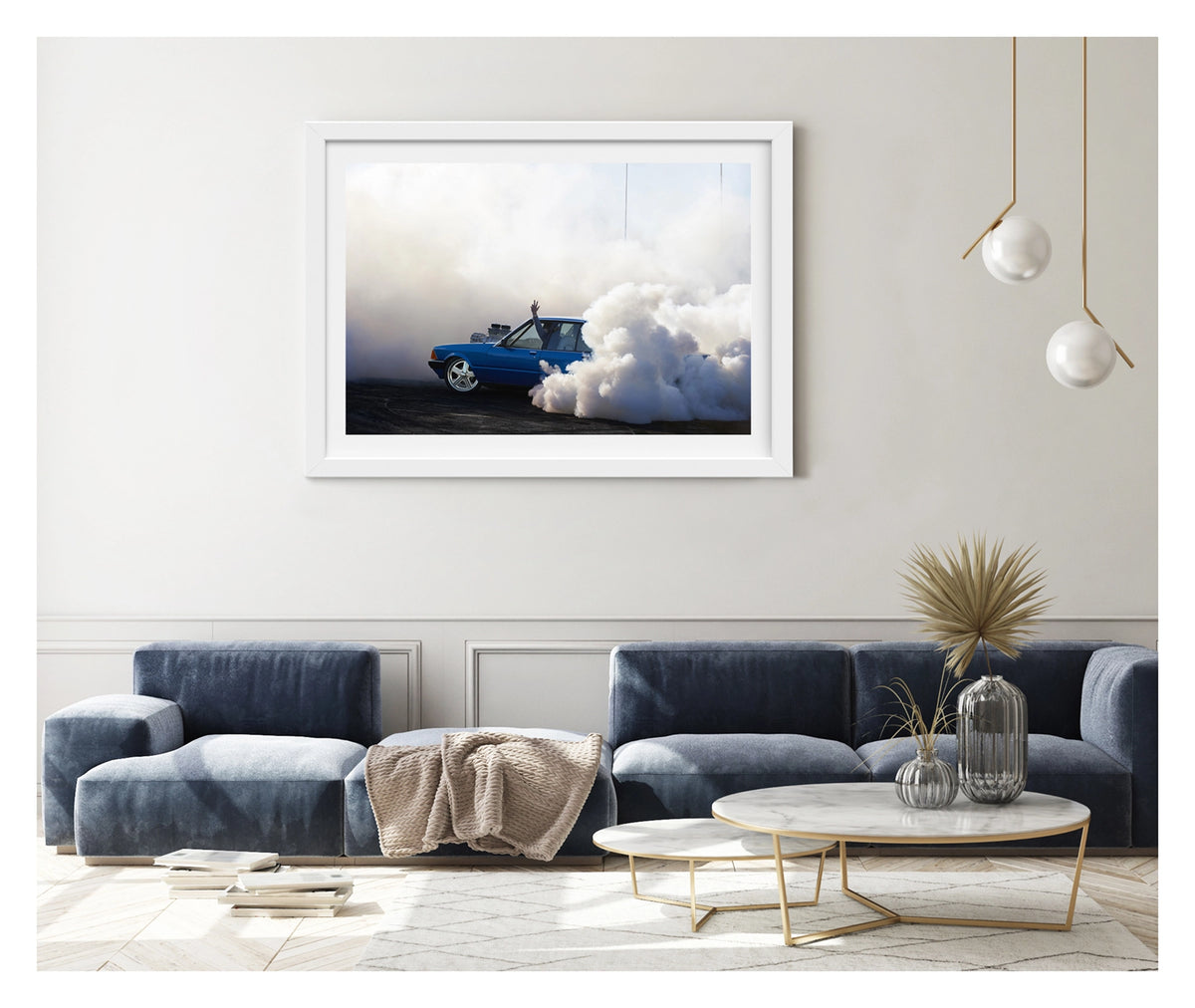 Framed in white, hanging in a contemporary space. A blue Ford XD Falcon sedan with a blown engine through the bonnet unleashes a burnout, a massive cloud of white tyre smoke engulfing the rear of the car and rolling across the tyre marked black bitumen. The passenger's arm reaches through the open window above the roofline as the bold blue body and polished five spoke wheels sit sharp against the billowing white smoke filling the frame. Fine art colour photographic print by Simon Davidson.