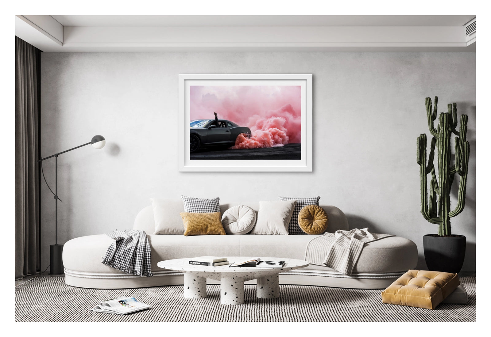 Framed in white, shown in a contemporary living space. A modern matte black Chevrolet Camaro performs a burnout, a dense cloud of pink tyre smoke erupting from the rear wheel and billowing across the tyre damaged black bitumen. The passenger's arm reaches through the open window with a single finger pointed skyward as the bold contrast of the dark body against the rolling pink smoke fills the frame. Fine art colour photographic print by Simon Davidson.