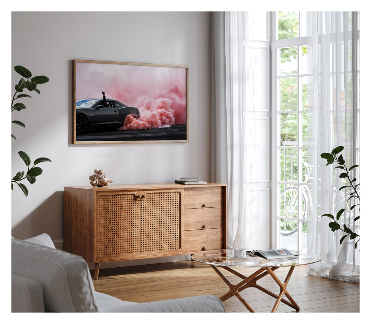 Framed in timber, shown in a contemporary living space. A modern matte black Chevrolet Camaro performs a burnout, a dense cloud of pink tyre smoke erupting from the rear wheel and billowing across the tyre damaged black bitumen. The passenger's arm reaches through the open window with a single finger pointed skyward as the bold contrast of the dark body against the rolling pink smoke fills the frame. Fine art colour photographic print by Simon Davidson.