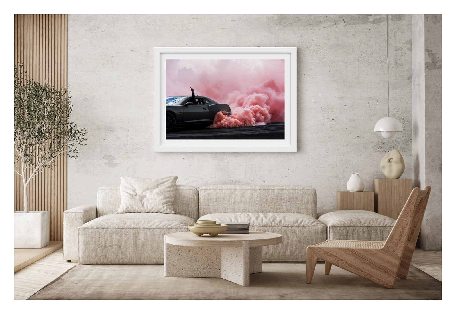 Framed in white, shown in a contemporary living space. A modern matte black Chevrolet Camaro performs a burnout, a dense cloud of pink tyre smoke erupting from the rear wheel and billowing across the tyre damaged black bitumen. The passenger's arm reaches through the open window with a single finger pointed skyward as the bold contrast of the dark body against the rolling pink smoke fills the frame. Fine art colour photographic print by Simon Davidson.