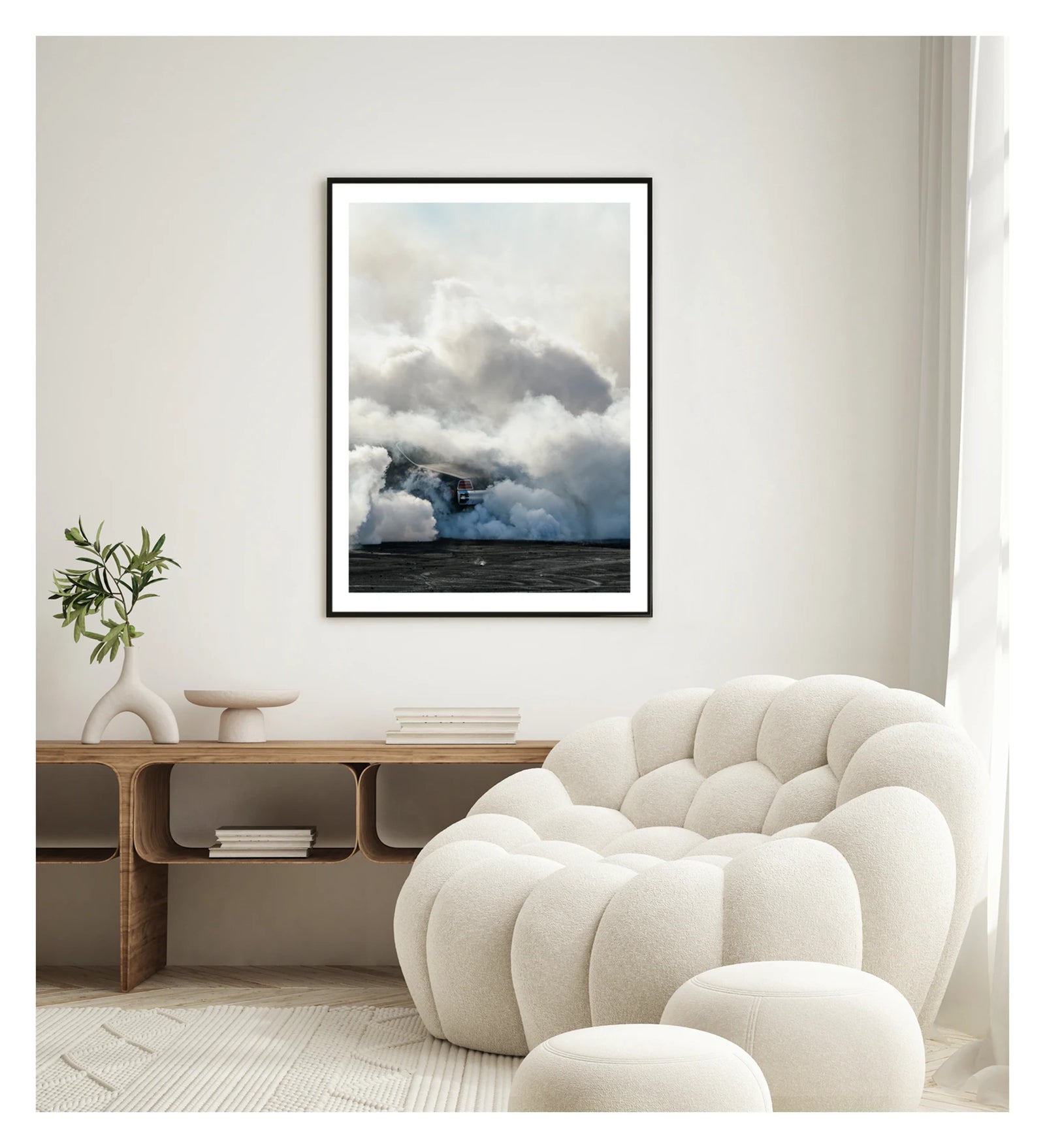 Framed in black, displayed in a contemporary living space. We see rear of a black Holden GTS sedan is almost entirely swallowed by a towering cloud of white tyre smoke during a burnout, with only the red tail light and rear chrome bumper visible through the billowing haze. The smoke builds into a massive marshmallow like formation that fills the frame from the black bitumen covered in burnout detritus to the pale sky above, dwarfing the car beneath it. Fine art colour photographic print by Simon Davidson.
