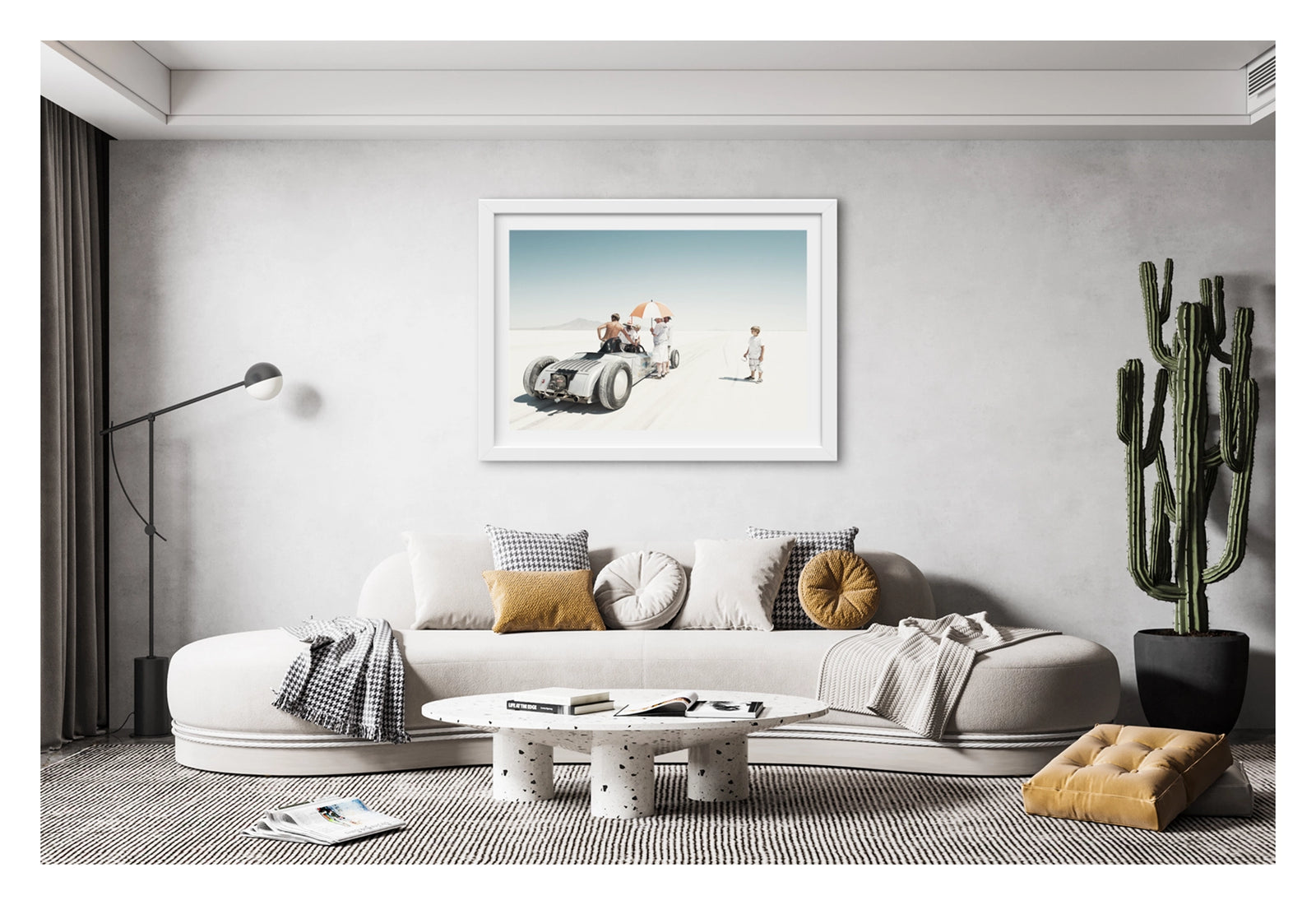 Framed in white, hanging in a contemporary space. We see a vintage landspeed race car waits on the start line of the Bonneville salt flats as crew members shelter beneath an umbrella. A young boy looks on. The scene floats in the vast white silence of the Bonneville salt lake. Fine art photograph by Simon Davidson