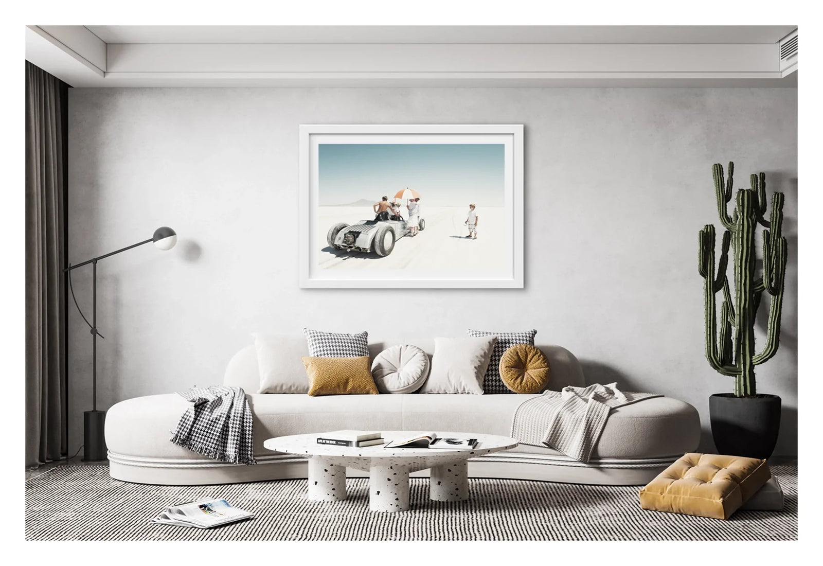 Framed in white, hanging in a contemporary space. We see a vintage landspeed race car waits on the start line of the Bonneville salt flats as crew members shelter beneath an umbrella. A young boy looks on. The scene floats in the vast white silence of the Bonneville salt lake. Fine art photograph by Simon Davidson