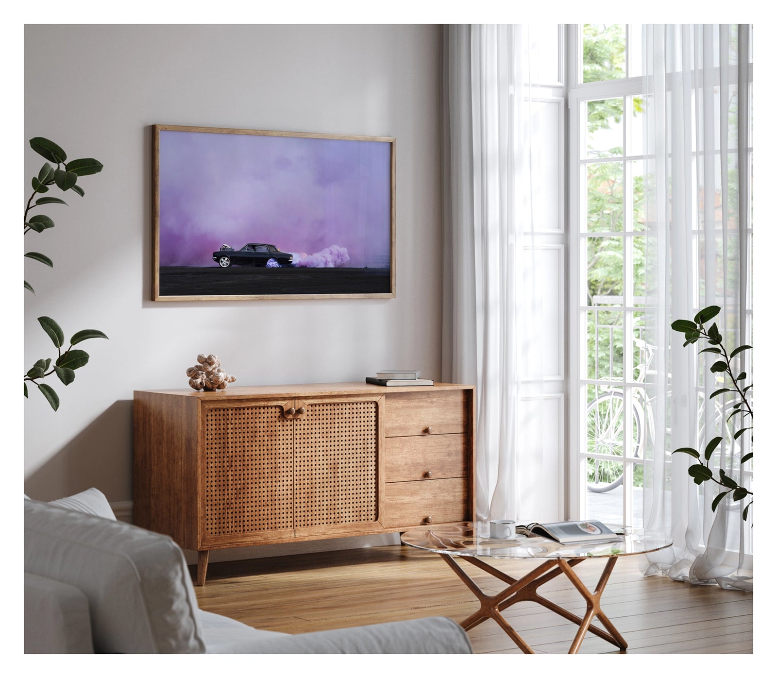 Framed in timber, shown in a contemporary living space. A black Holden chrome bumper sedan with an exposed supercharger out the bonnet performs a burnout on a vast black bitumen surface, trailing a long rolling cloud of billowing purple tyre smoke that sweeps across the right side of the frame and fills the entire sky behind. The car sits small and sharp against the expansive purple haze, the scene feeling open and cinematic in its scale. Fine art colour photographic print by Simon Davidson.