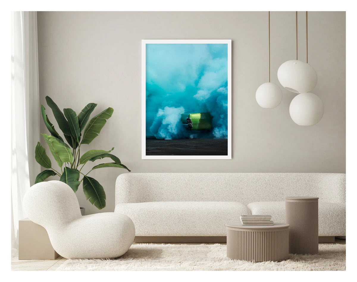 Framed in white, in a portrait orientation. The rear of metallic green Valiant Regal is almost completely consumed by a vast billowing cloud of vivid teal tyre smoke during a burnout. The electric contrast of the bright green body against the churning aqua smoke creates a striking abstract quality, the car appearing to float above the scorched black bitumen below. Framed print shown in a contemporary room. Fine art colour photographic print by Simon Davidson.