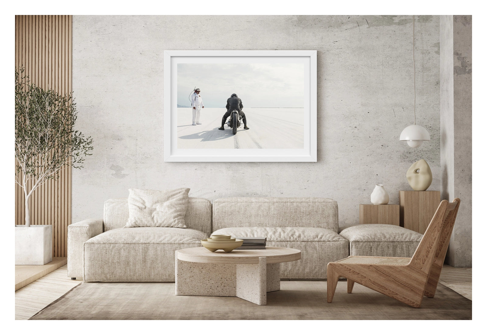 Framed in white hanging in a contemporary living space. Motorcycle racer Shinya Kimura in black leathers crouches low over his vintage custom motorcycle on the Bonneville Salt Flats, poised at the start of a run as tyre tracks stretch toward the vanishing point ahead. A race official in a white jumpsuit and radio headset stands to the left watching on, the vast white salt and pale overcast sky dissolving into a seamless horizon in the distance. Fine art colour photographic print by Simon Davidson.
