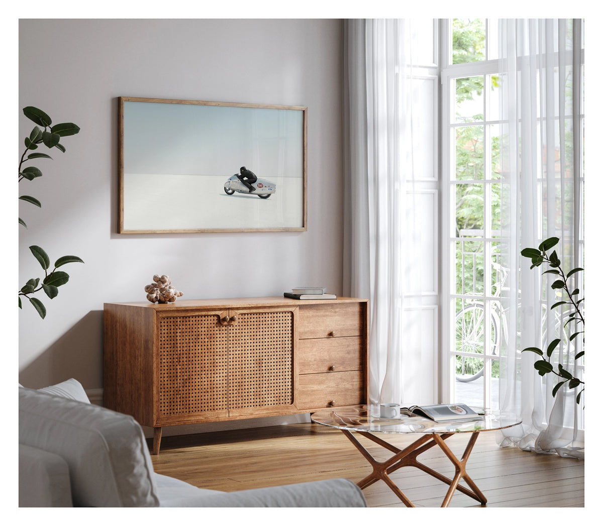 Framed in timber, shown in a contemporary living space is a black leather clad rider crouching low over a bare metal aluminium streamliner motorcycle numbered 1141 as it races across the vast white expanse of the bonneville  salt flats The rider and machine are small but in striking form against the pale horizon and soft blue sky above. The hand beaten metal bike and minimal silhouette give the scene a timeless, sculptural quality as it pushes across the featureless white surface. Fine art colour photograph