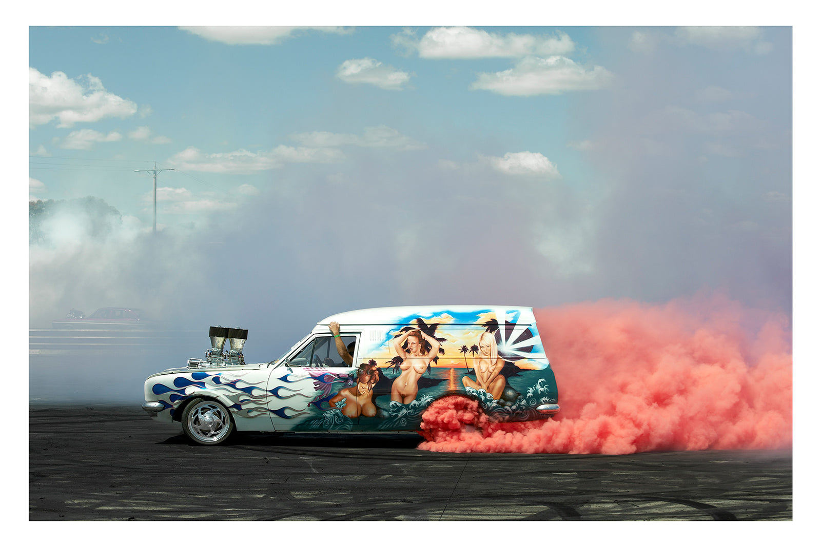 A heavily customised Australian panel van with an elaborate tropical mural and blue flame paintwork lays down a burnout under a blue sky with scattered clouds, pink tyre smoke erupting from the rear wheels and trailing behind as white smoke drifts across the left side of the frame. Supercharger protrudes through the bonnet. The lavishly painted side panel depicting a sunset beach scene in 1970s van culture glory. Fine art photographic print by Simon Davidson.