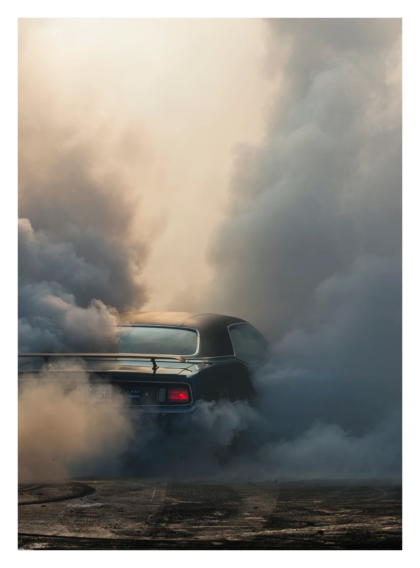 Captured in a portrait orientation.  We see the rear of a black Plymouth Barracuda with a vinyl roof performing a burnout, almost entirely consumed by billowing clouds of tyre smoke that fill the frame from ground to sky. A single red tail light glows through the haze as rubber marks streak the bitumen below. Fine art colour photographic print by Simon Davidson.