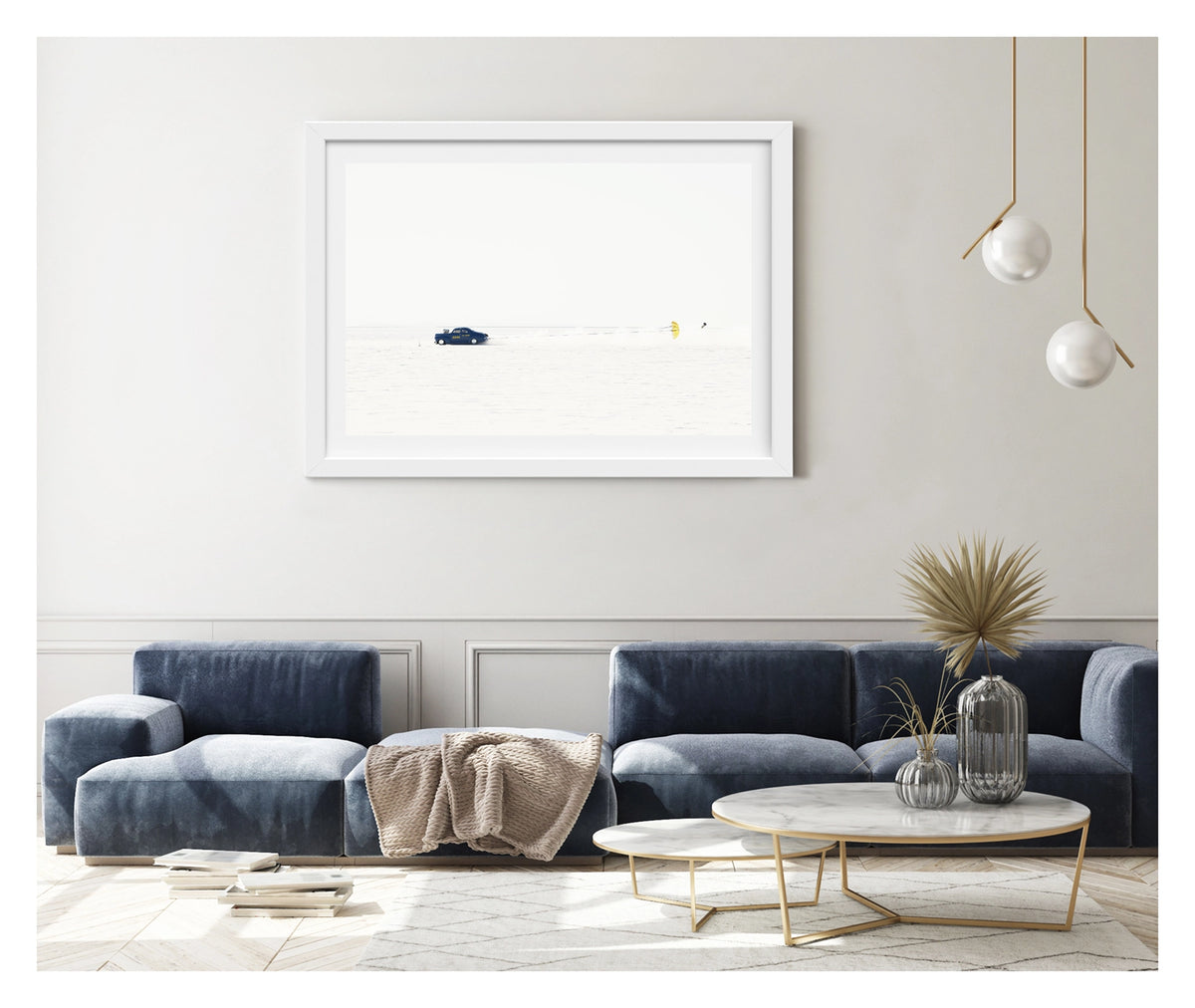 Framed in white, shown in a contemporary living space. A dark blue 1940s coupe landspeed race car numbered releases a bright yellow parachute to slow down after a high speed run across the Bonneville Salt Flats, the chute billowing open behind it as a trail of disturbed salt dust follows in its wake. The car and chute sit as tiny vivid forms against the vast featureless white of the salt and sky, the scene almost entirely bleached of colour. Fine art colour photographic print by Simon Davidson.