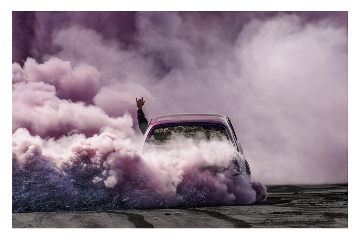 A purple Torana slides through the scene, rear to camera, is all but consumed by a vast billowing cloud of vivid purple smoke, with a passenger's arm thrust through the window throwing devil horns above the roofline as the only sign of human life within the haze. Fine art colour photographic print by Simon Davidson.