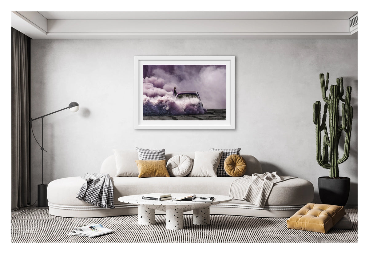 Framed in white, shown in a contemporary living space we see a purple Torana as it slides through the scene, rear to camera, is all but consumed by a vast billowing cloud of vivid purple smoke, with a passenger's arm thrust through the window throwing devil horns above the roofline as the only sign of human life within the haze. Fine art colour photographic print by Simon Davidson.