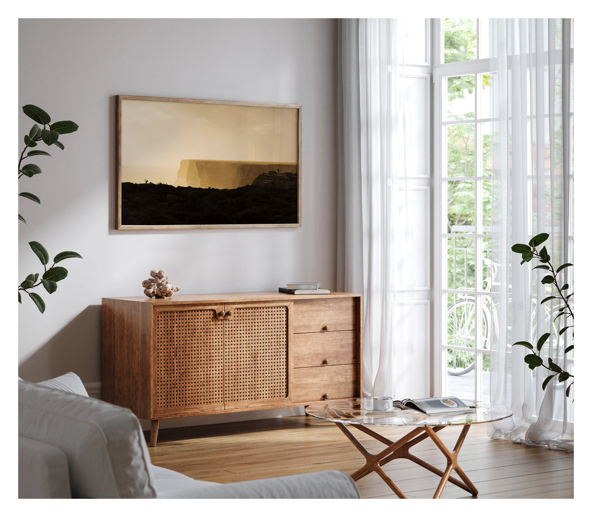 Framed in timber, shown in a contemporary living space. We see in the distance a lone figure standing at the edge of the towering limestone cliffs of the Great Australian Bight, rendered as a tiny silhouette against the warm golden light of dusk. The sheer cliff face stretches across the frame above a hazy Southern Ocean, the dark scrubby foreground in deep shadow while the sky and sea glow in rich amber and gold. Fine art colour photographic print by Simon Davidson.