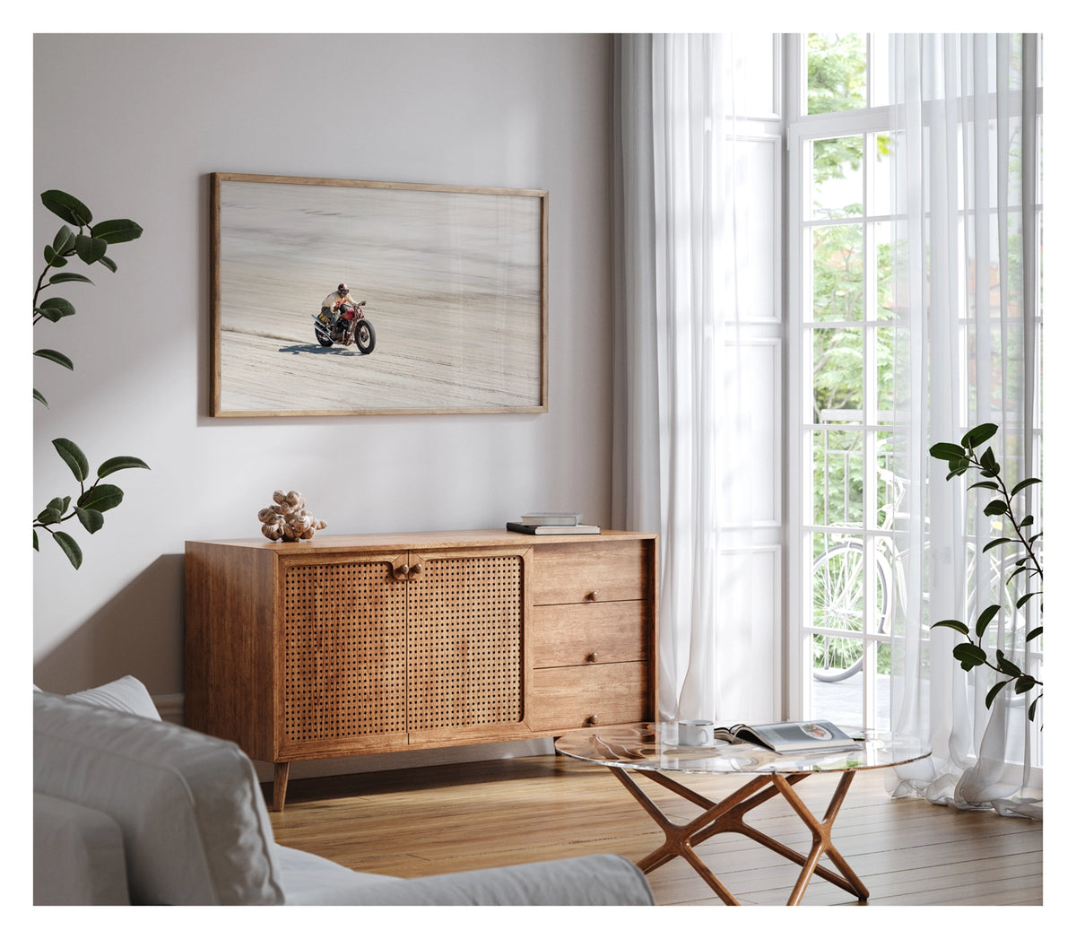 Framed in timber, shown in a contemporary space. Photographed from above a motorcycle racer in a cream sweater, goggles and open face helmet leans forward over a red pre-war vintage Harley Davidson as it races down the beach., a small trail of sand kicking up behind as the bike accelerates across the textured surface. Fine art colour photographic print by Simon Davidson.