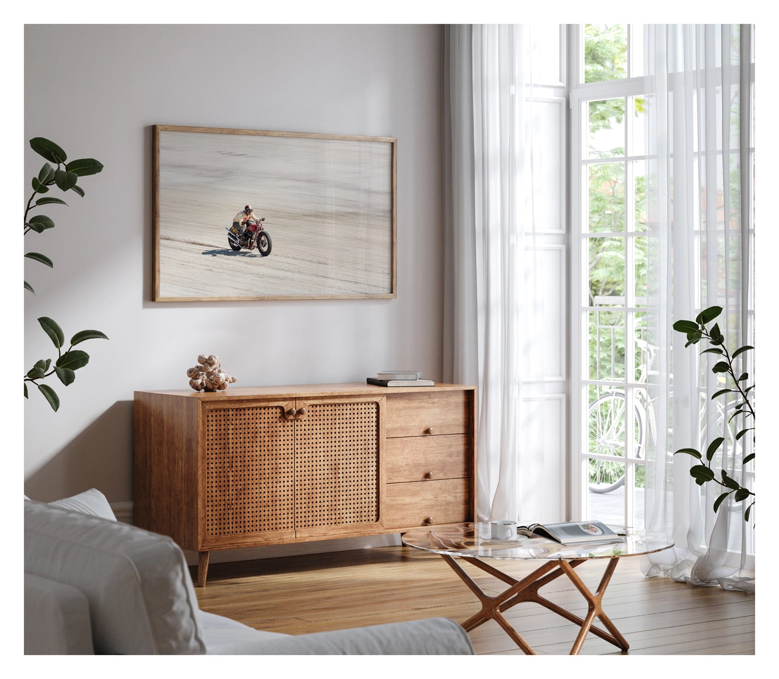 Framed in timber, shown in a contemporary space. Photographed from above a motorcycle racer in a cream sweater, goggles and open face helmet leans forward over a red pre-war vintage Harley Davidson as it races down the beach., a small trail of sand kicking up behind as the bike accelerates across the textured surface. Fine art colour photographic print by Simon Davidson.