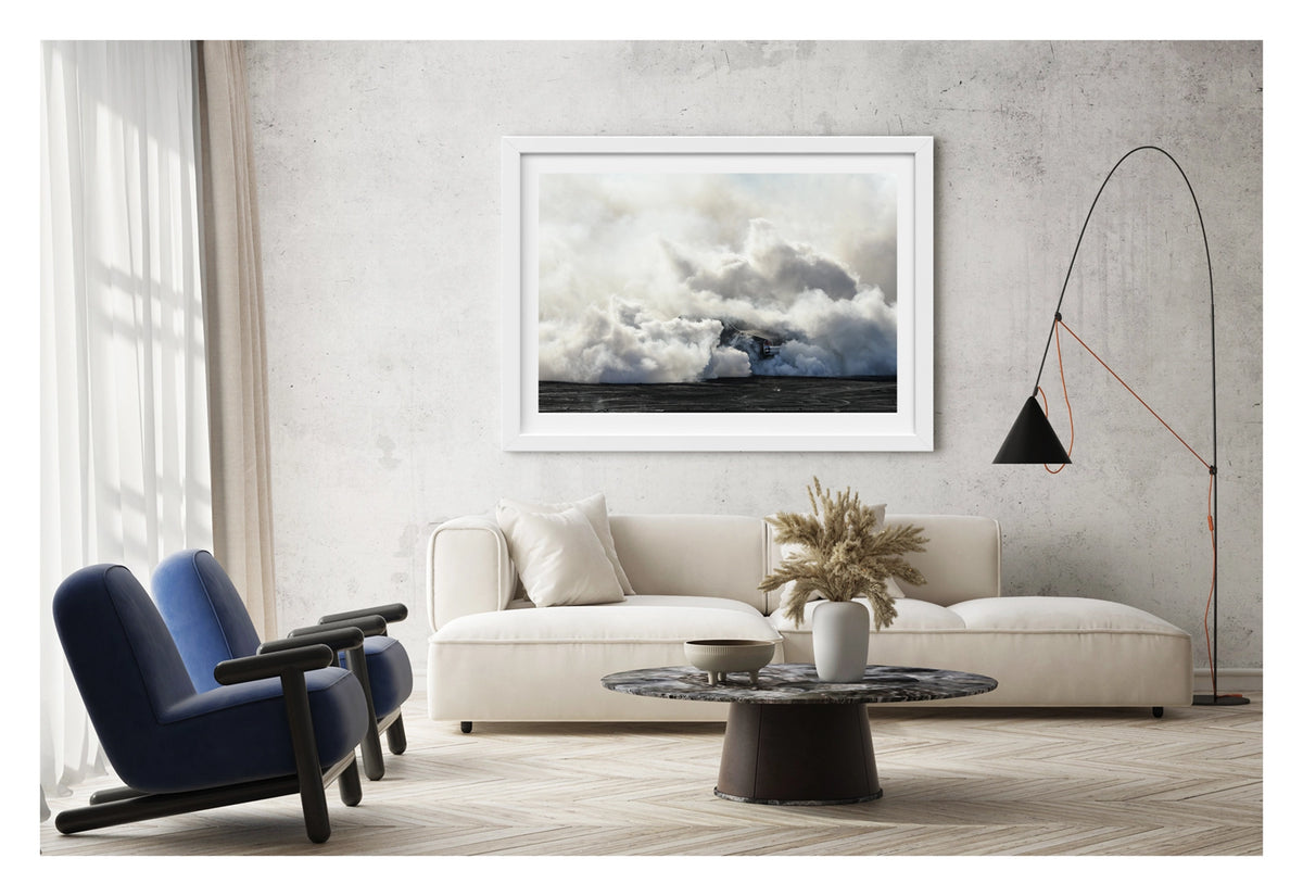 Framed in white, displayed in a contemporary living space. The rear of a black Holden GTS sedan is almost entirely swallowed by a towering cloud of white tyre smoke during a burnout, with only the red tail light and rear chrome bumper visible through the billowing haze. The smoke builds into a massive marshmallow like formation that fills the frame from the black bitumen covered in burnout detritus to the pale sky above, dwarfing the car beneath it. Fine art colour photographic print by Simon Davidson.
