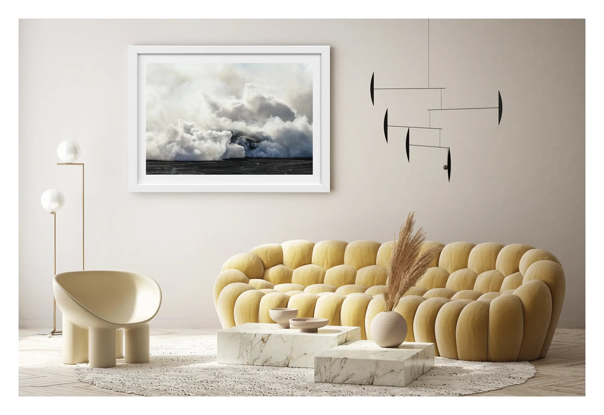Framed in white, displayed in a contemporary living space. We see rear of a black Holden GTS sedan is almost entirely swallowed by a towering cloud of white tyre smoke during a burnout, with only the red tail light and rear chrome bumper visible through the billowing haze. The smoke builds into a massive marshmallow like formation that fills the frame from the black bitumen covered in burnout detritus to the pale sky above, dwarfing the car beneath it. Fine art colour photographic print by Simon Davidson.
