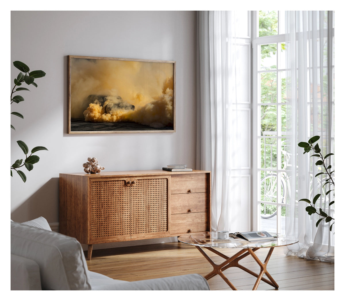 Framed in timber, shown in a contemporary living space. A black Holden Holden sedan is almost near consumed by a towering cloud of deep amber and orange tyre smoke that fills the entire frame, the roofline and windscreen barely visible through the churning golden haze. The warm orange smoke billows dramatically in every direction across the marked black bitumen, giving the scene an almost volcanic intensity. Fine art colour photographic print by Simon Davidson.