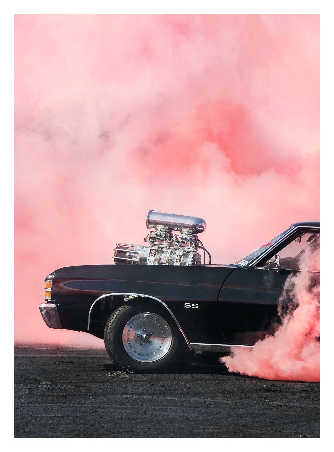A black Chevrolet Chevelle SS with a massive polished supercharger protruding through the bonnet performs a burnout, engulfed in vivid pink tyre smoke that fills the entire background. The chrome blower and intake manifold gleam against the dark body as thick pink smoke pours from the under the car onto the tyre marked scorched black bitumen. Fine art colour photographic print by Simon Davidson.