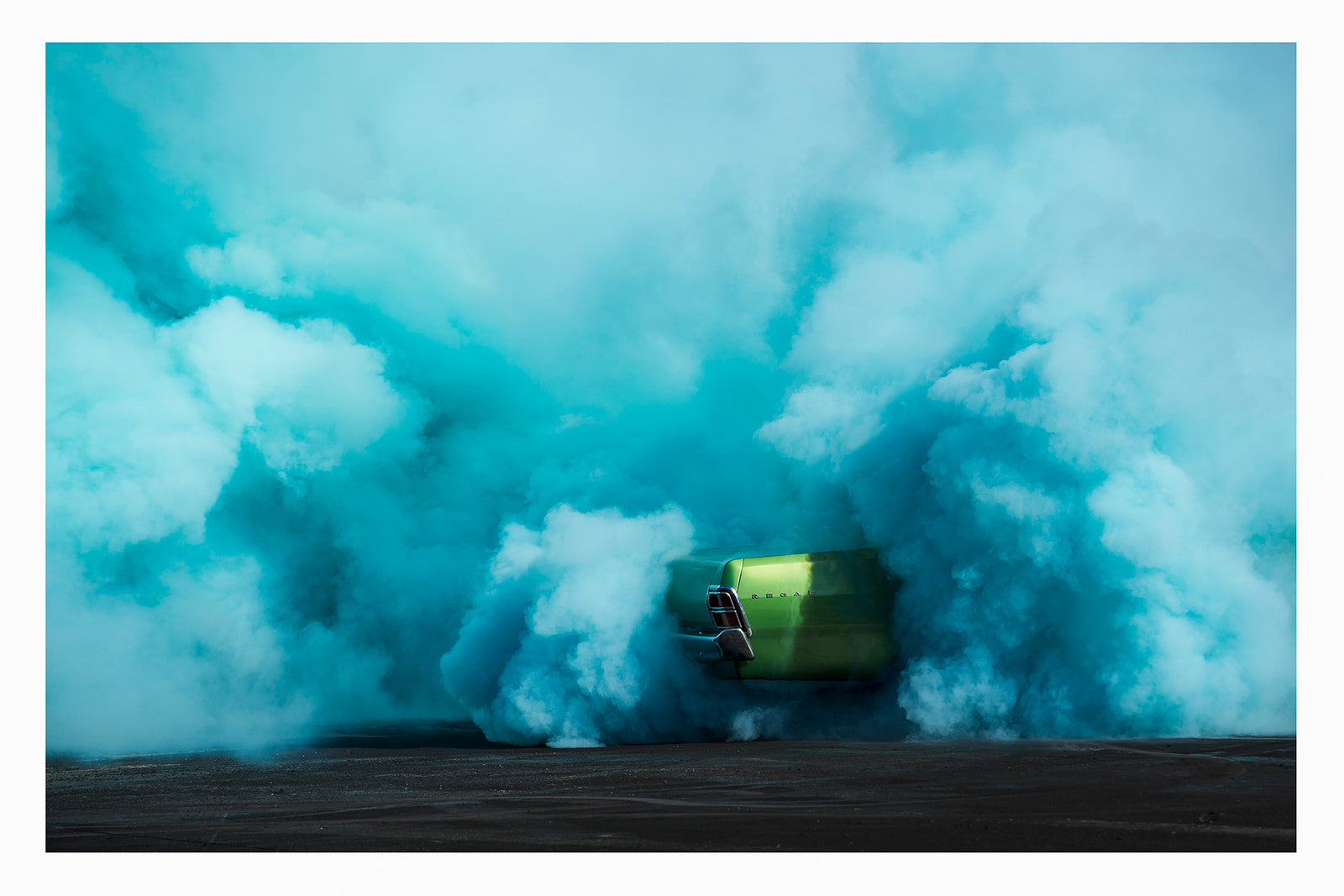 The rear of metallic green Valiant Regal is almost completely consumed by a vast billowing cloud of vivid teal tyre smoke during a burnout. The electric contrast of the bright green body against the churning aqua smoke creates a striking abstract quality, the car appearing to float above the scorched black bitumen below. Fine art colour photographic print by Simon Davidson.