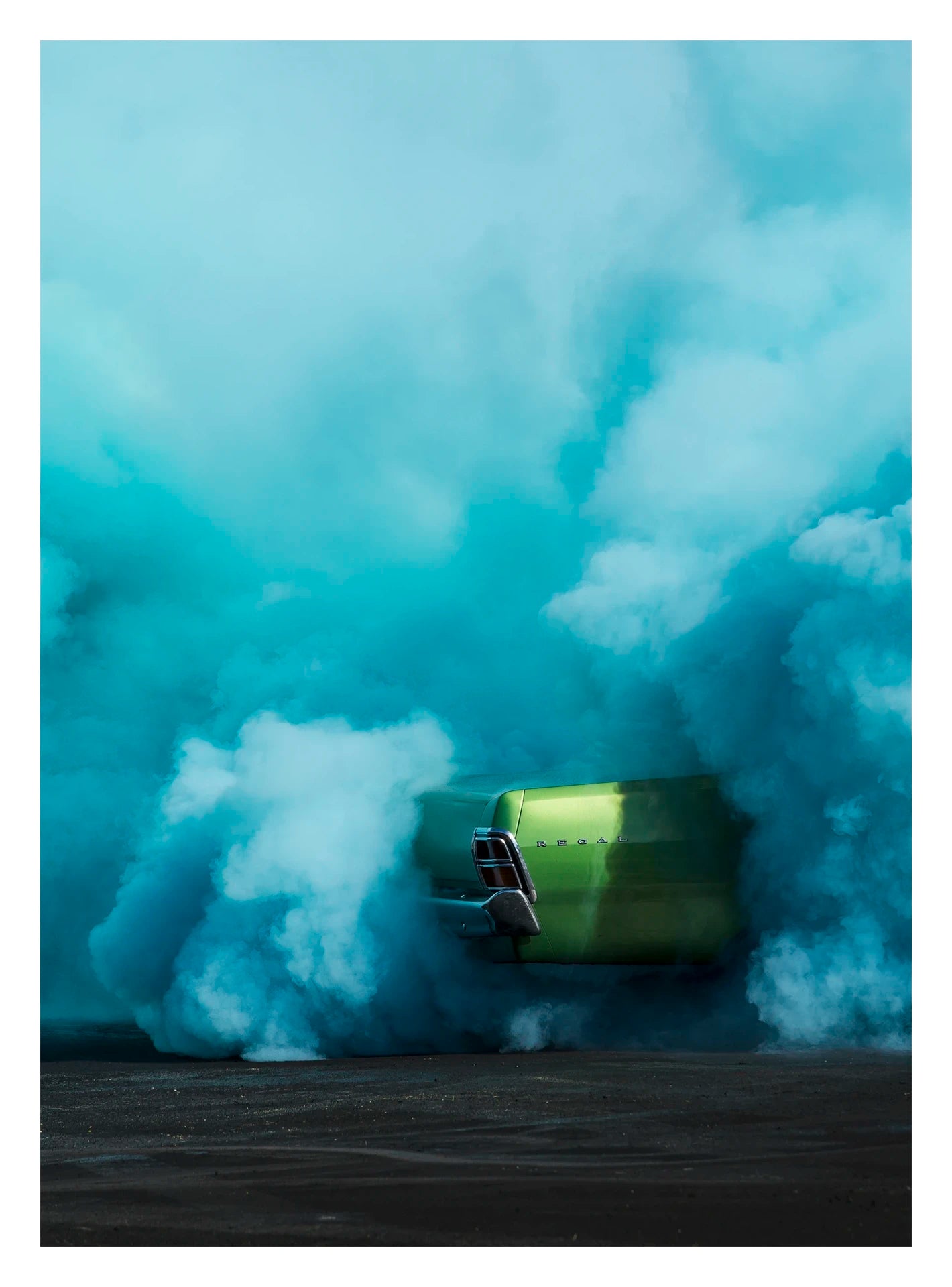 Captured in a portrait orientation. The rear of metallic green Valiant Regal is almost completely consumed by a vast billowing cloud of vivid teal tyre smoke during a burnout. The electric contrast of the bright green body against the churning aqua smoke creates a striking abstract quality, the car appearing to float above the scorched black bitumen below. Fine art colour photographic print by Simon Davidson.