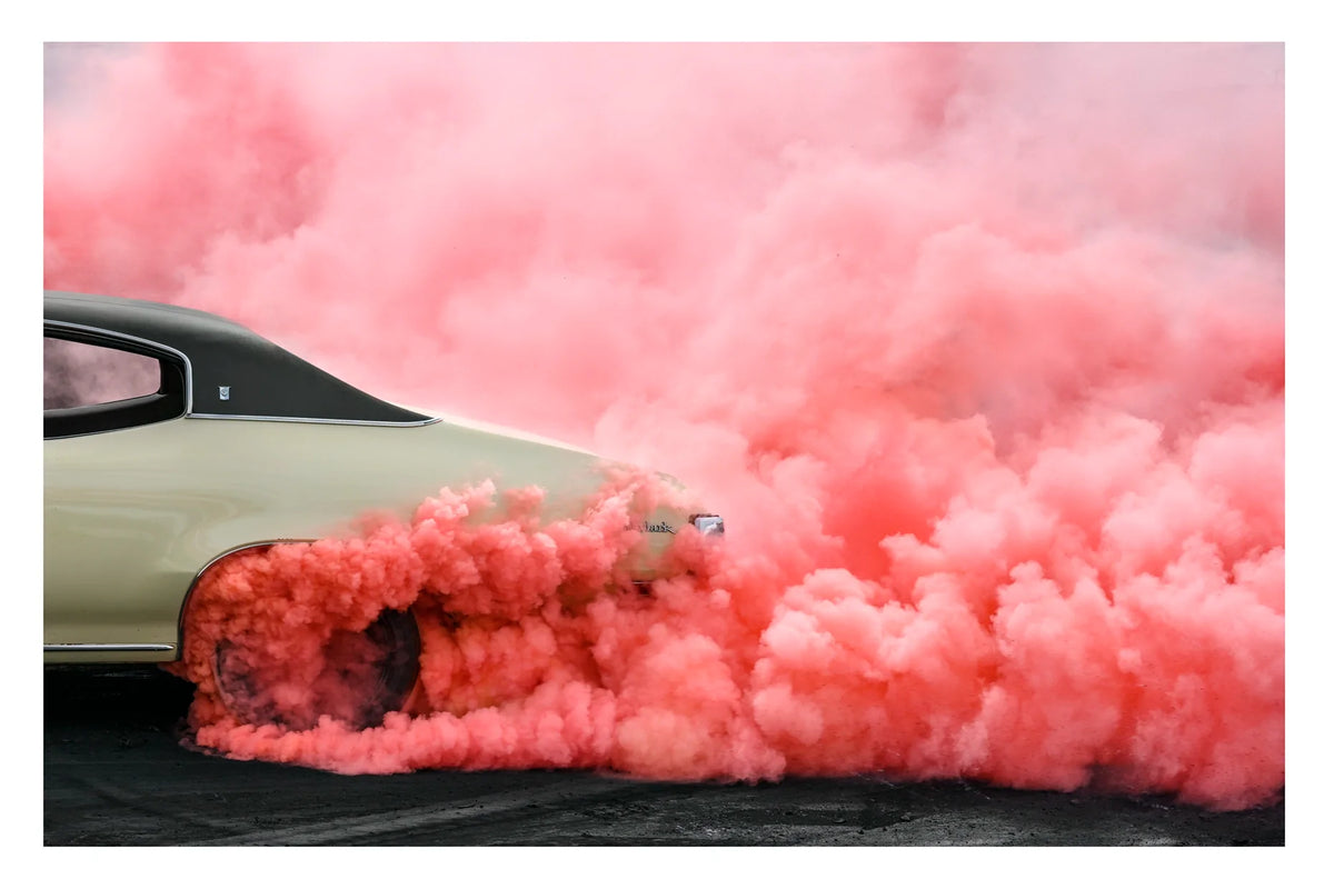 Rear side quarter of a metallic gold Buick SKYLARK, with black vinyl roof performs a burnout, engulfed in a dense rolling cloud of vivid watermelon coloured tyre smoke that billows across the entire right side of the frame. The smoke erupts from beneath the rear wheel arch and sweeps dramatically across the scorched black bitumen, the gold body and dark vinyl roof barely visible through the churning watermelon haze. Fine art colour photographic print by Simon Davidson.
