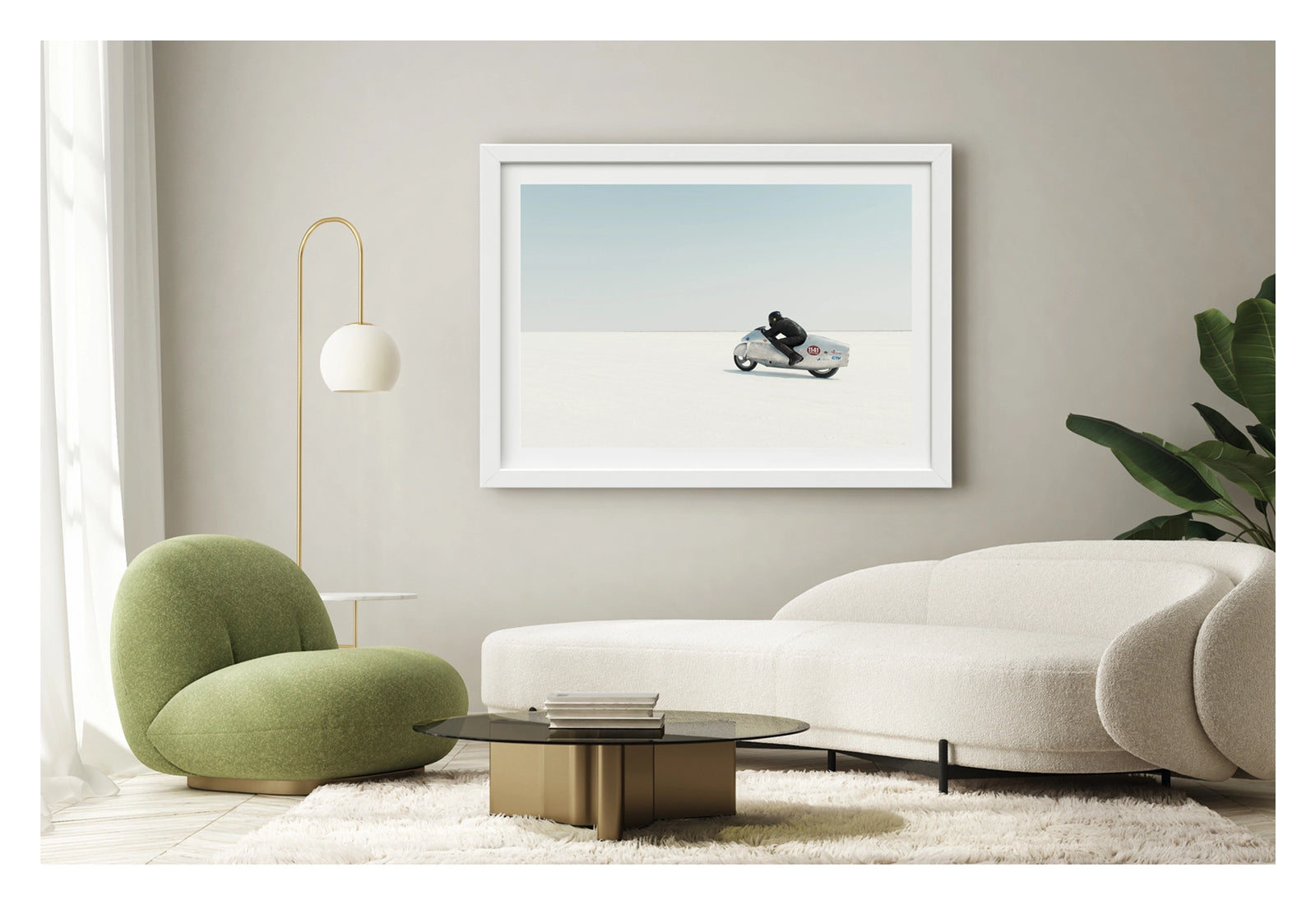 Framed in white, shown in a contemporary living space is a black leather clad rider crouching low over a bare metal aluminium streamliner motorcycle numbered 1141 as it races across the vast white expanse of the bonneville  salt flats The rider and machine are small but in striking form against the pale horizon and soft blue sky above. The hand beaten metal bike and minimal silhouette give the scene a timeless, sculptural quality as it pushes across the featureless white surface. Fine art colour photograph.
