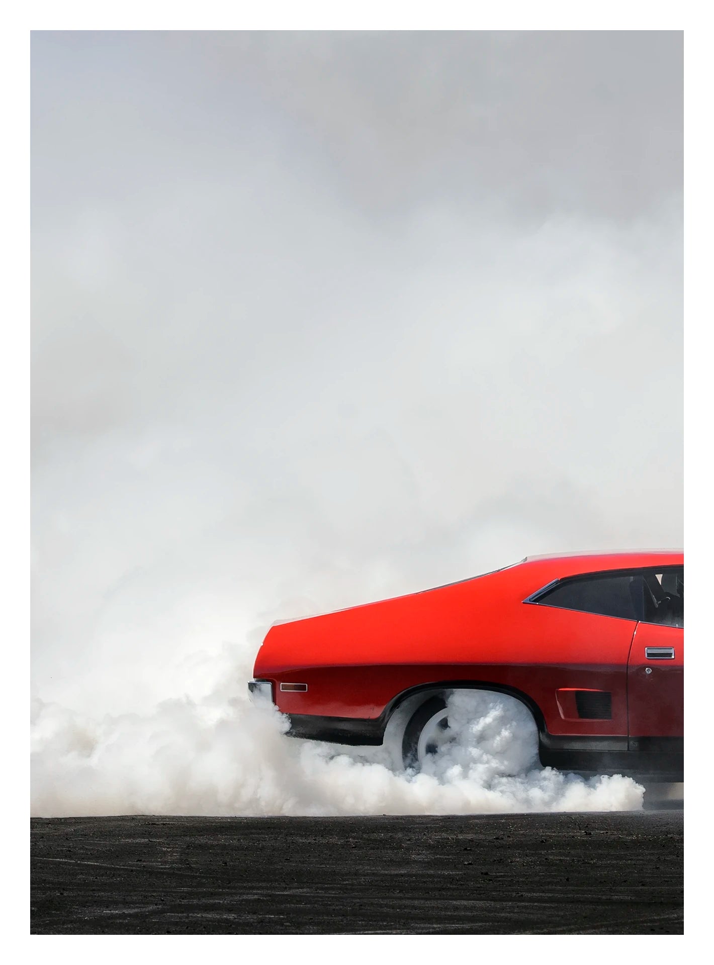 Captured in a portrait orientation. A red Ford Falcon XB coupe performs a burnout, shown is the back half of the car with dense white tyre smoke pouring from the rear wheels and engulfing the lower half of the car against a white smoke filled sky. The bold red bodywork and fastback roofline sit in sharp contrast to the billowing white smoke rolling across the scorched black bitumen below. Fine art colour photographic print by Simon Davidson.
